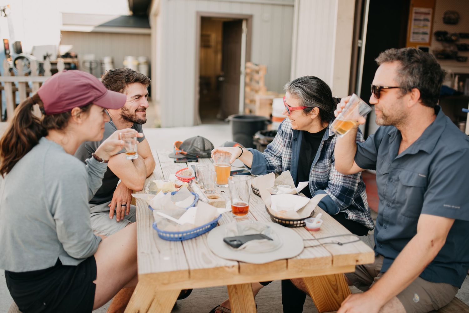 Group of friends enjoying food and drinks together at outdoor picnic table patio dining.