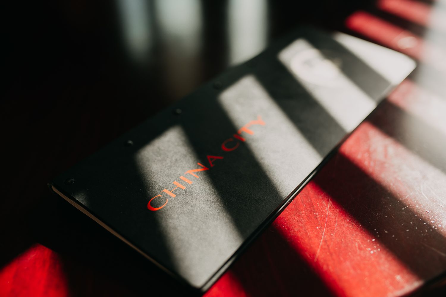 Black China City restaurant menu card resting on a red surface with dramatic shadow stripes.