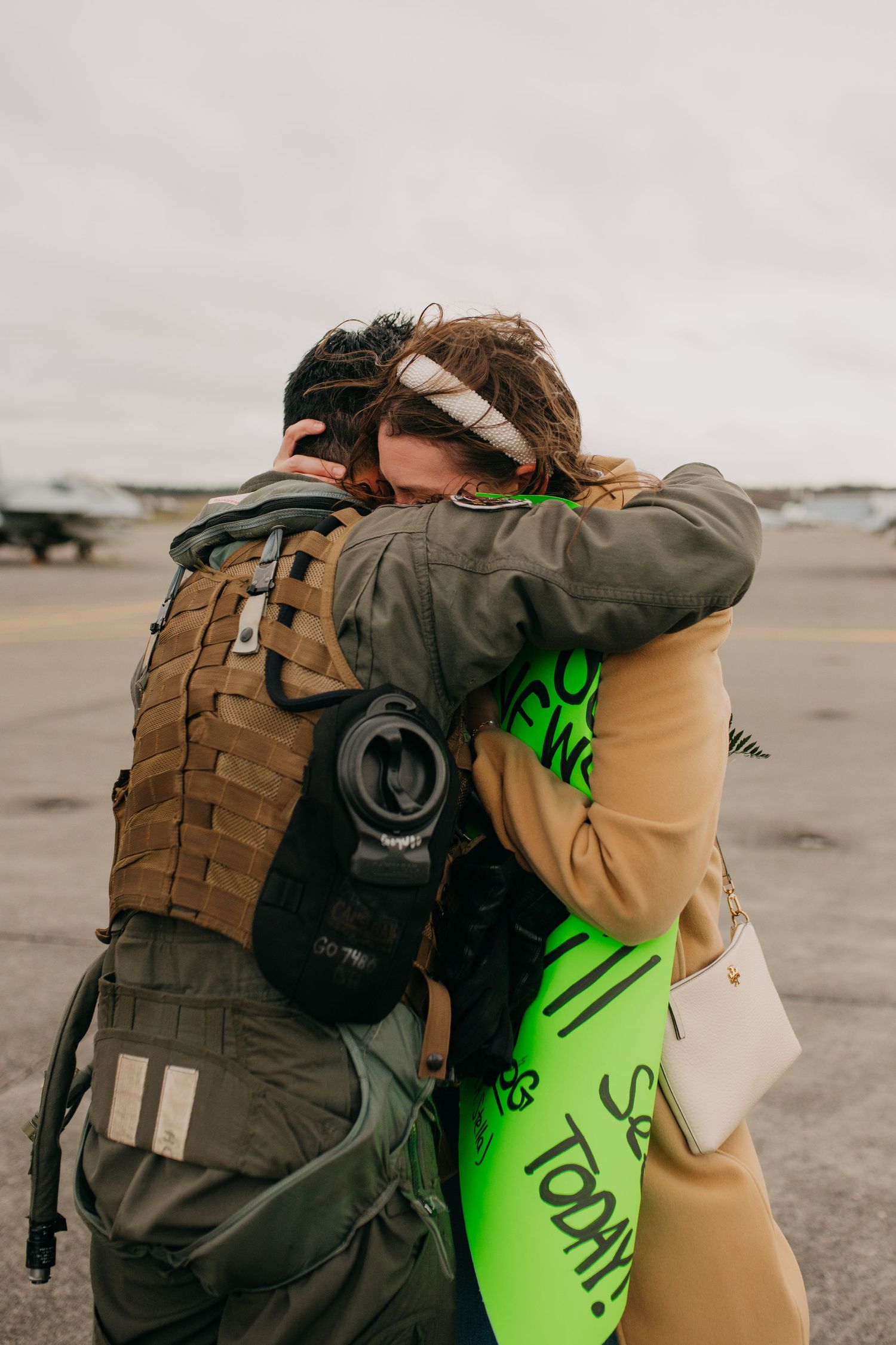 Emotional military homecoming reunion as soldier in tactical gear embraces loved one on airport tarmac.
