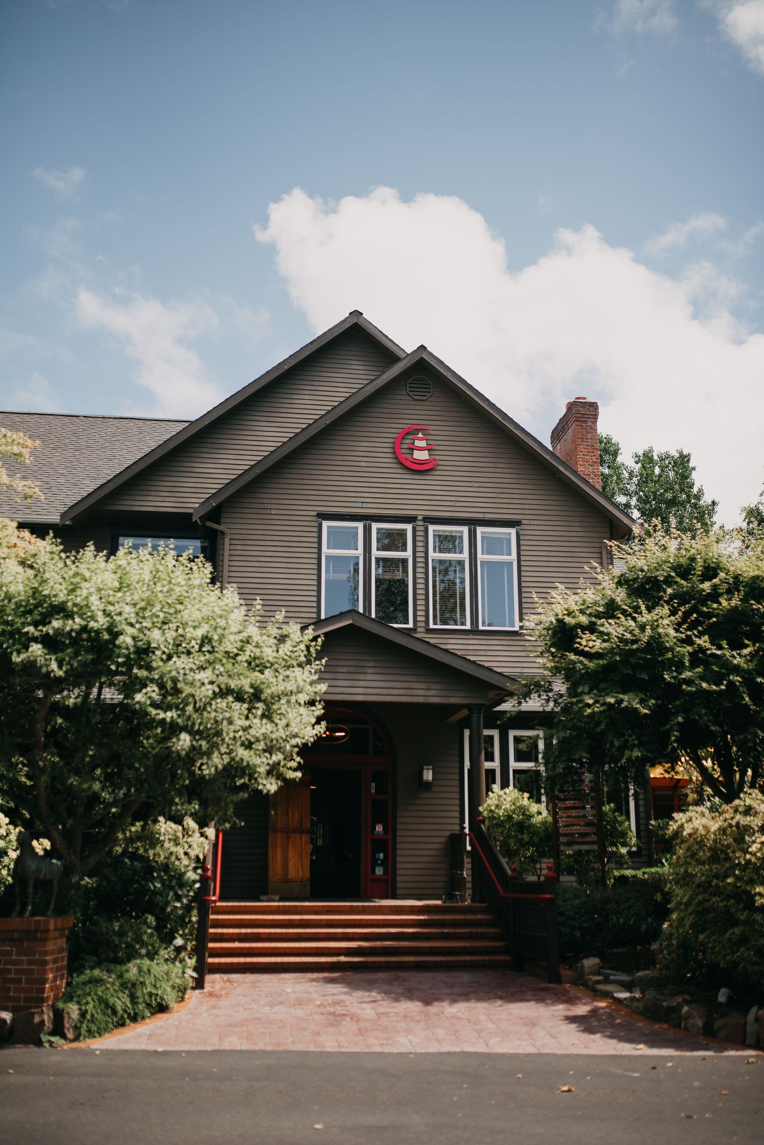 Charming craftsman-style restaurant exterior with olive green siding, red steps, and lush landscaping.