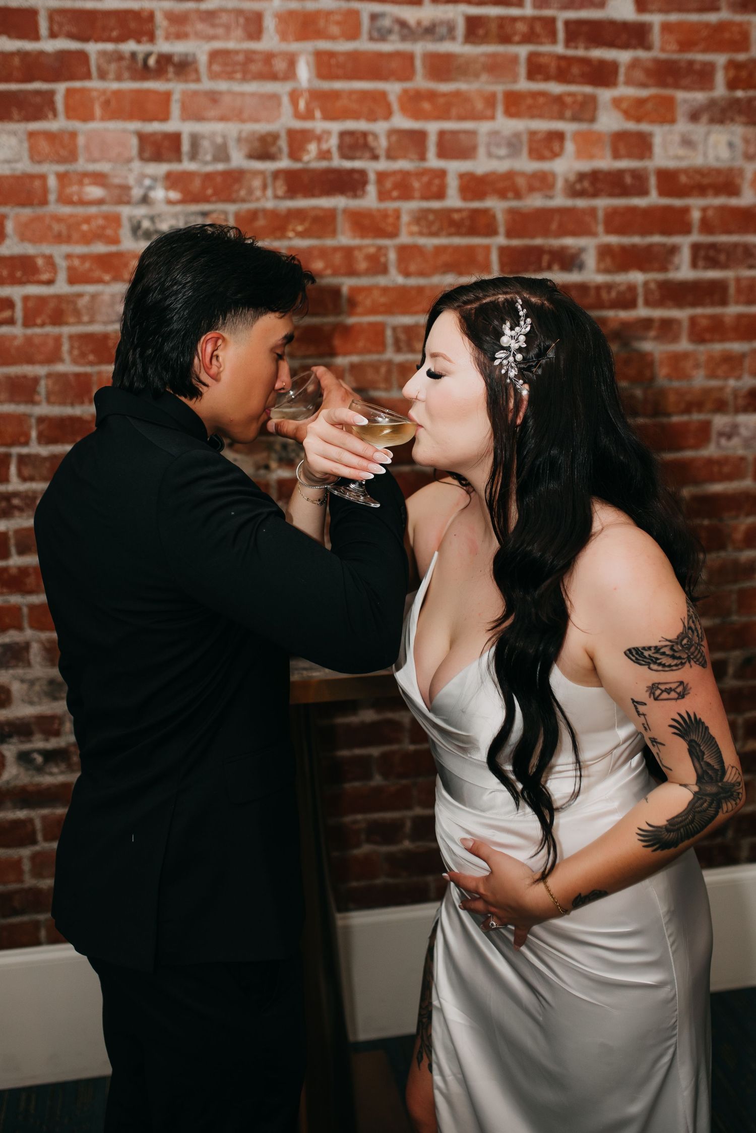 Bride and groom perform a romantic champagne toast in front of an exposed brick wall at their reception.
