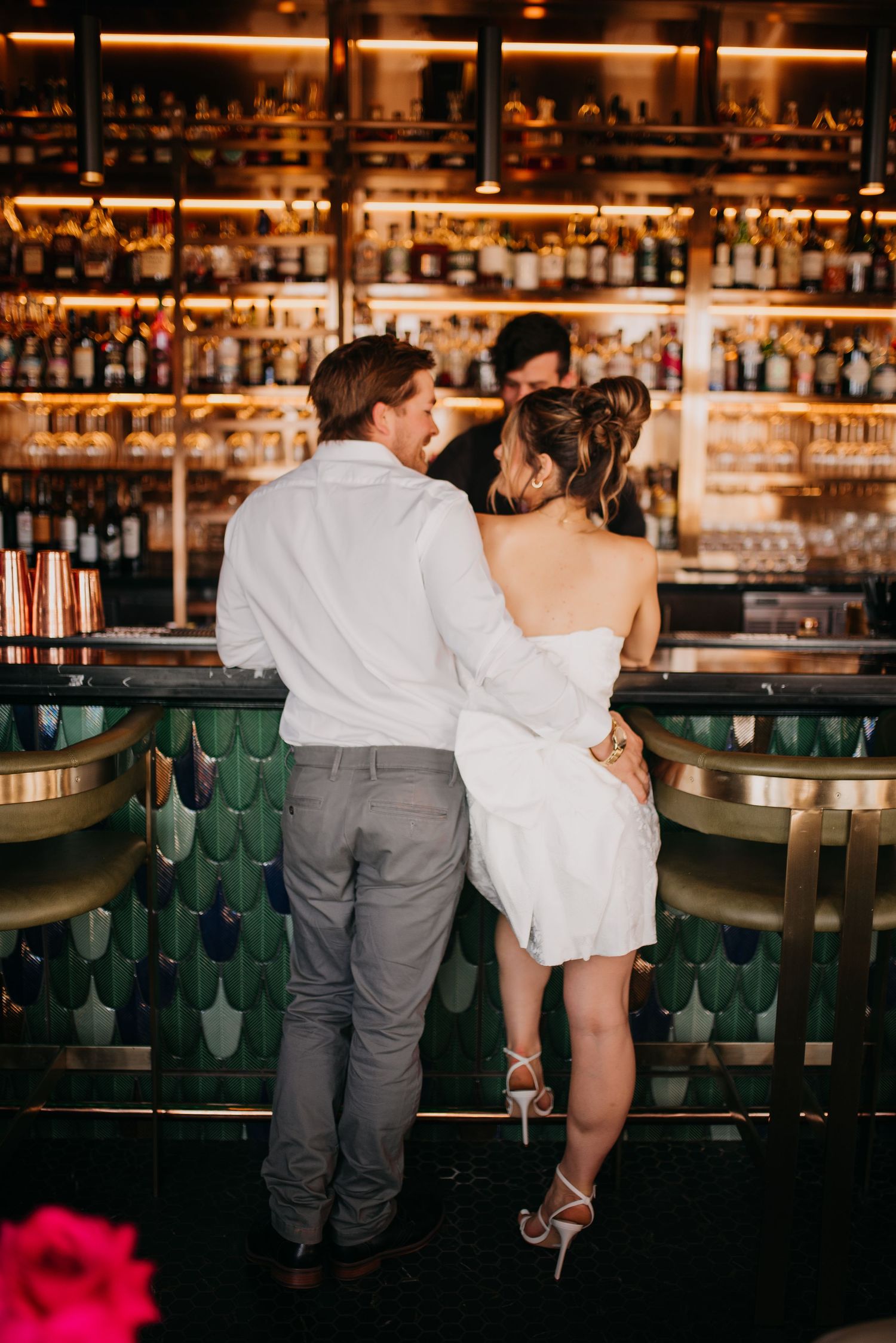 Bride and groom share intimate moment together at elegant gold and green wedding reception bar.
