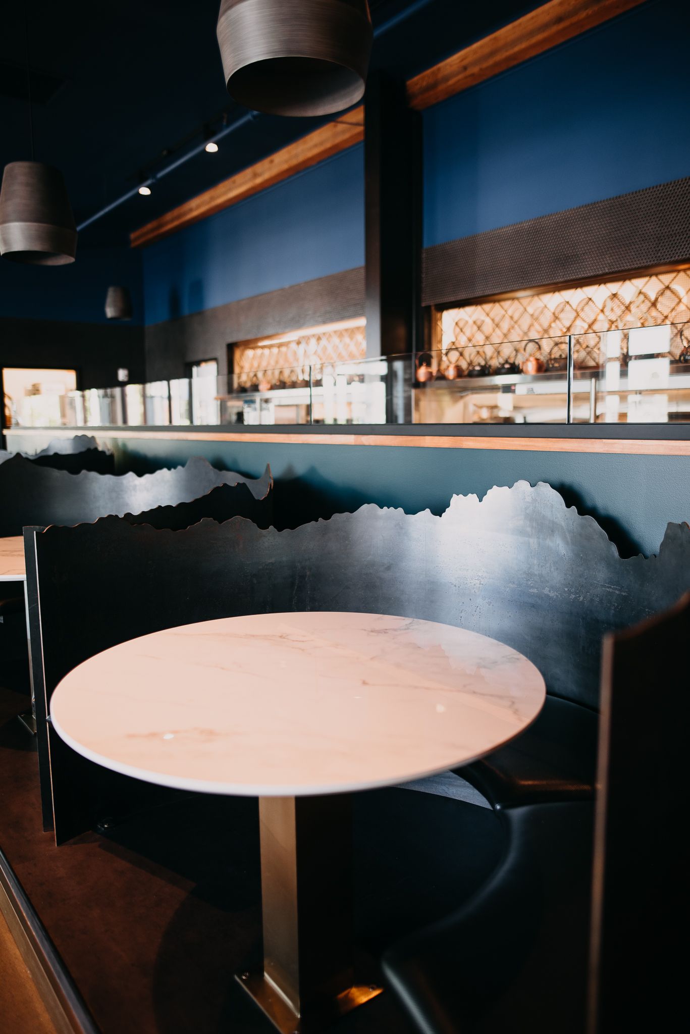 Modern restaurant interior with dark blue walls, marble table and decorative mountain silhouette.
