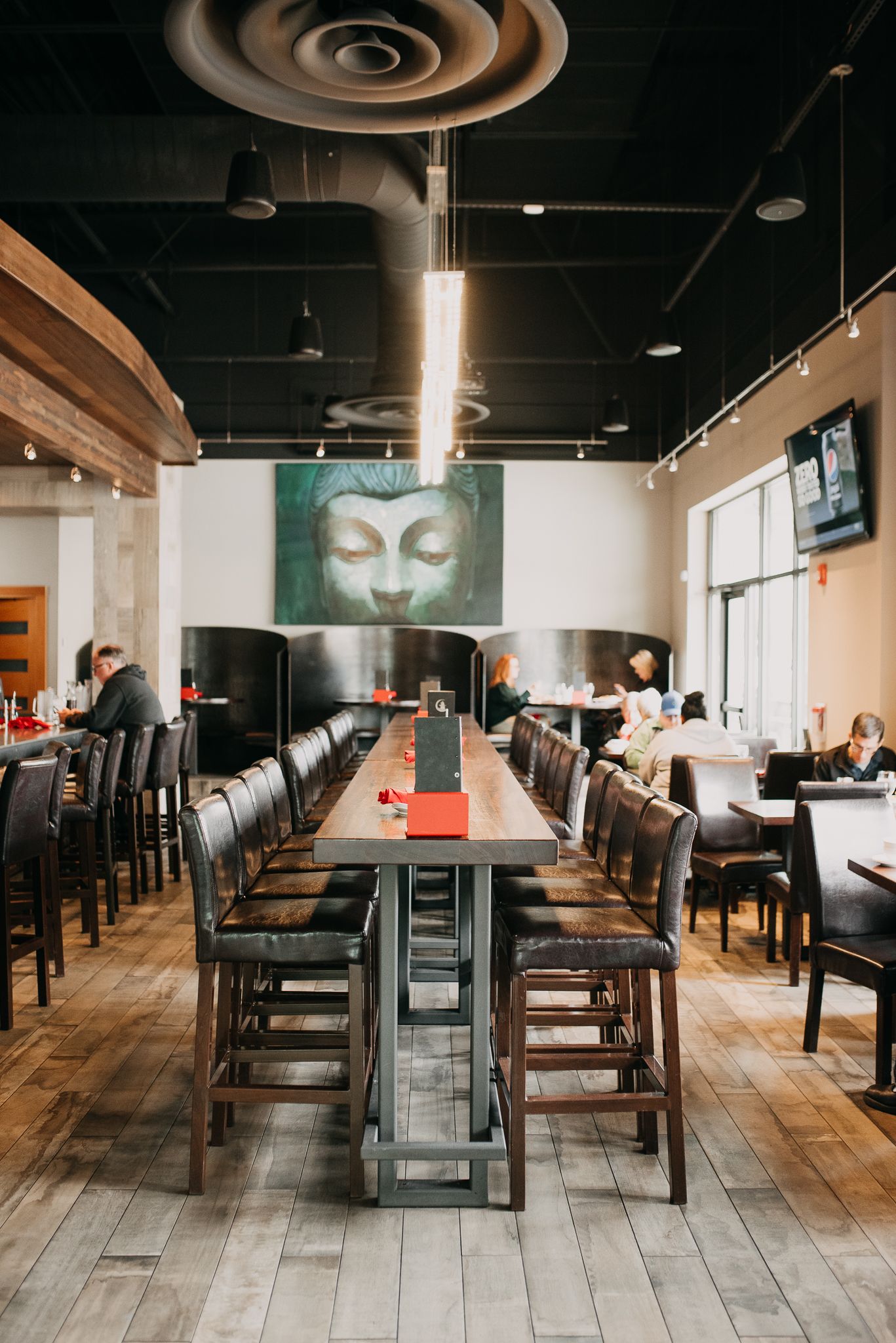 Modern Asian restaurant interior with long communal table, Buddha wall art, and industrial black ceiling.