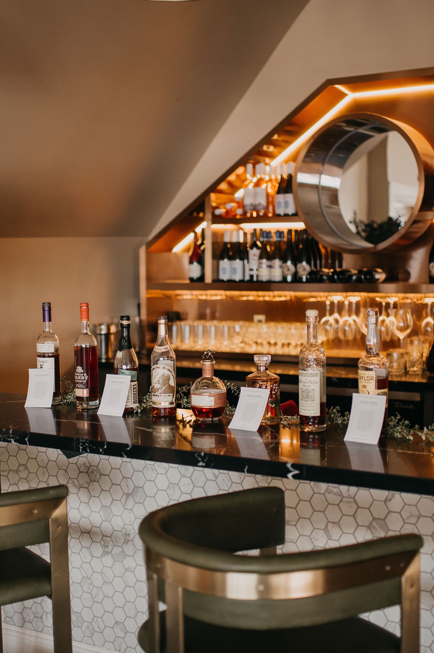 Elegant wedding bar setup with labeled spirit bottles, hexagon tile counter, and warm amber lighting.