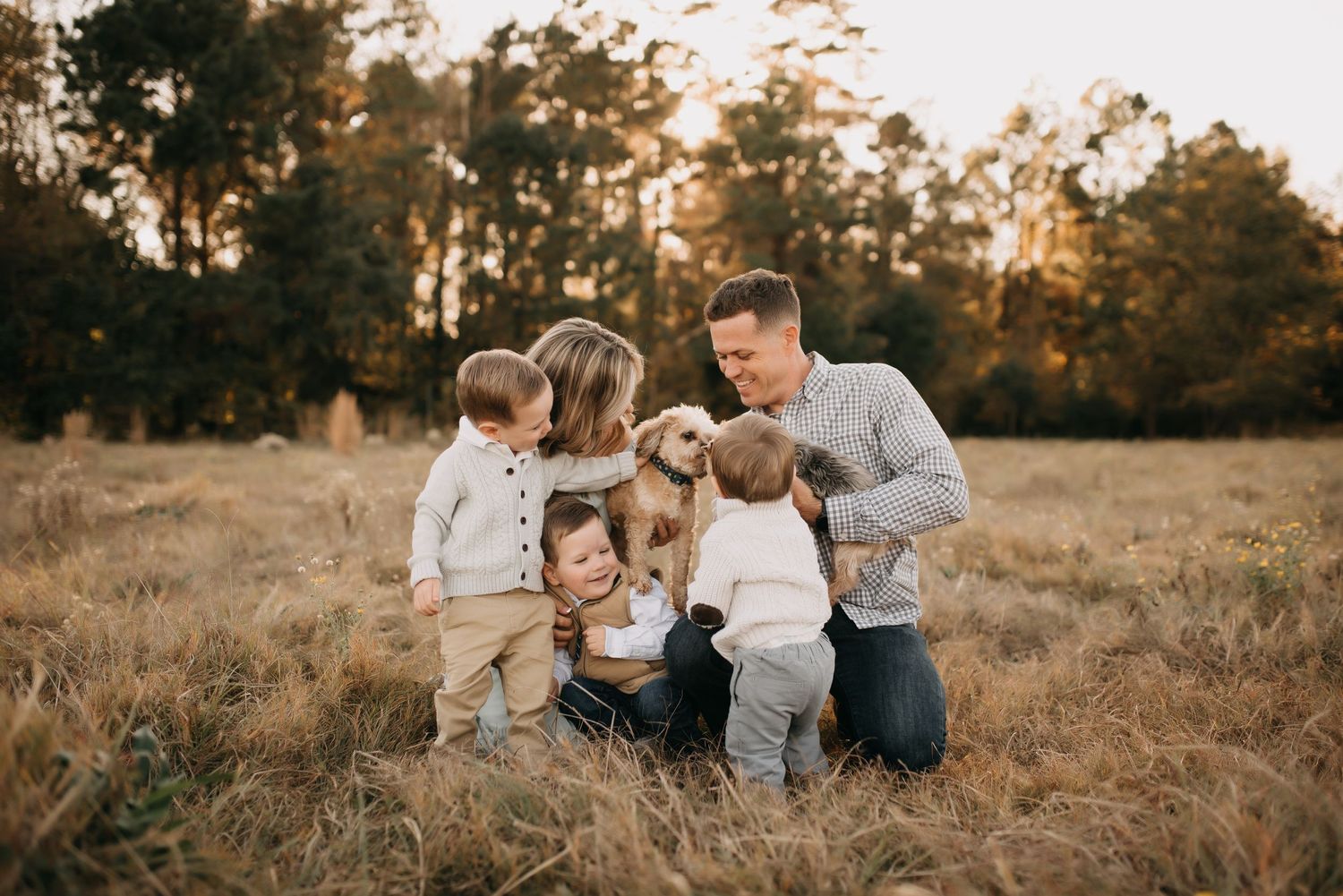 Happy family with three young children and a golden puppy sitting together in a sunlit autumn field.