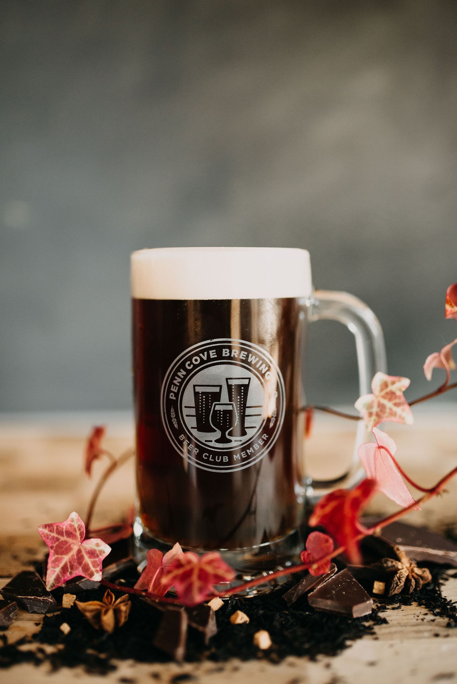 A dark craft beer in a Penn Cove Brewing mug club glass surrounded by chocolate and autumn foliage.