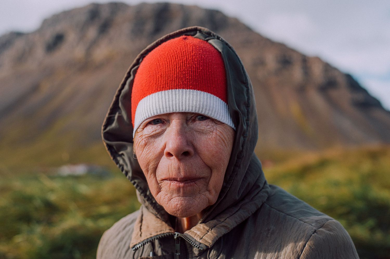 Portrait of an elderly person wearing a red and white beanie hat with mountains behind them.