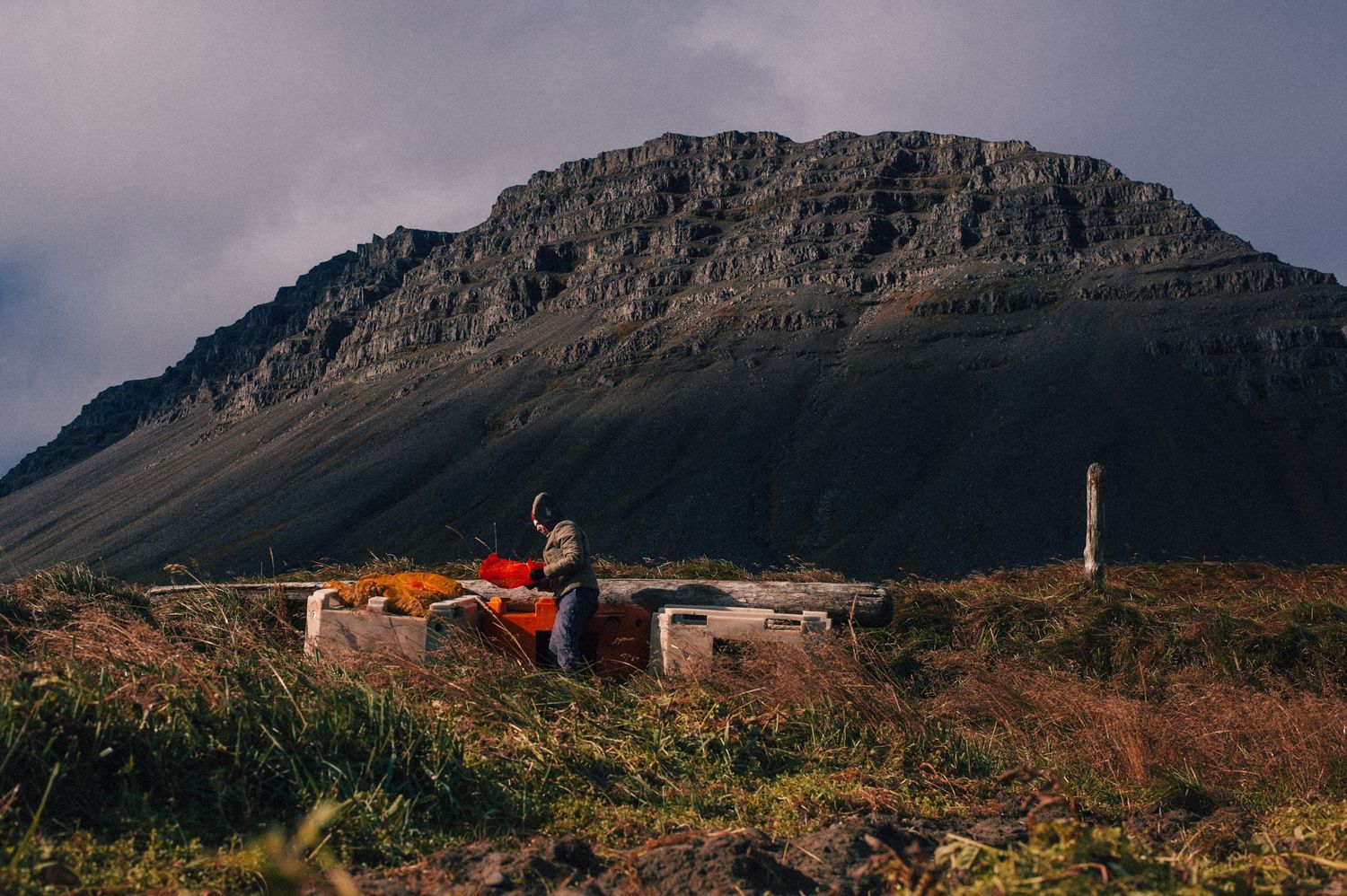 A person sits on a stone structure with colorful gear beneath a dramatic rocky mountain peak.