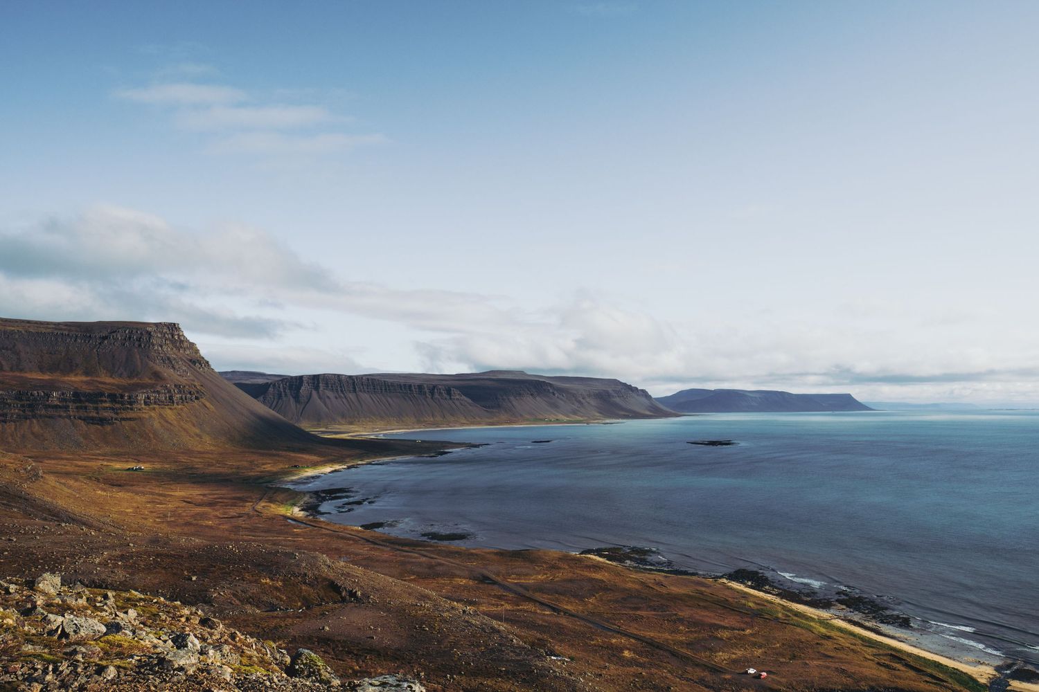 Panoramic view of rugged Icelandic Westfjords coastline with dramatic cliffs, brown terrain, and calm blue ocean waters.