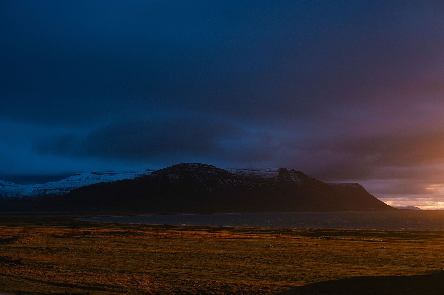A dark dramatic mountain silhouette glows under stormy skies at golden hour on open plains.