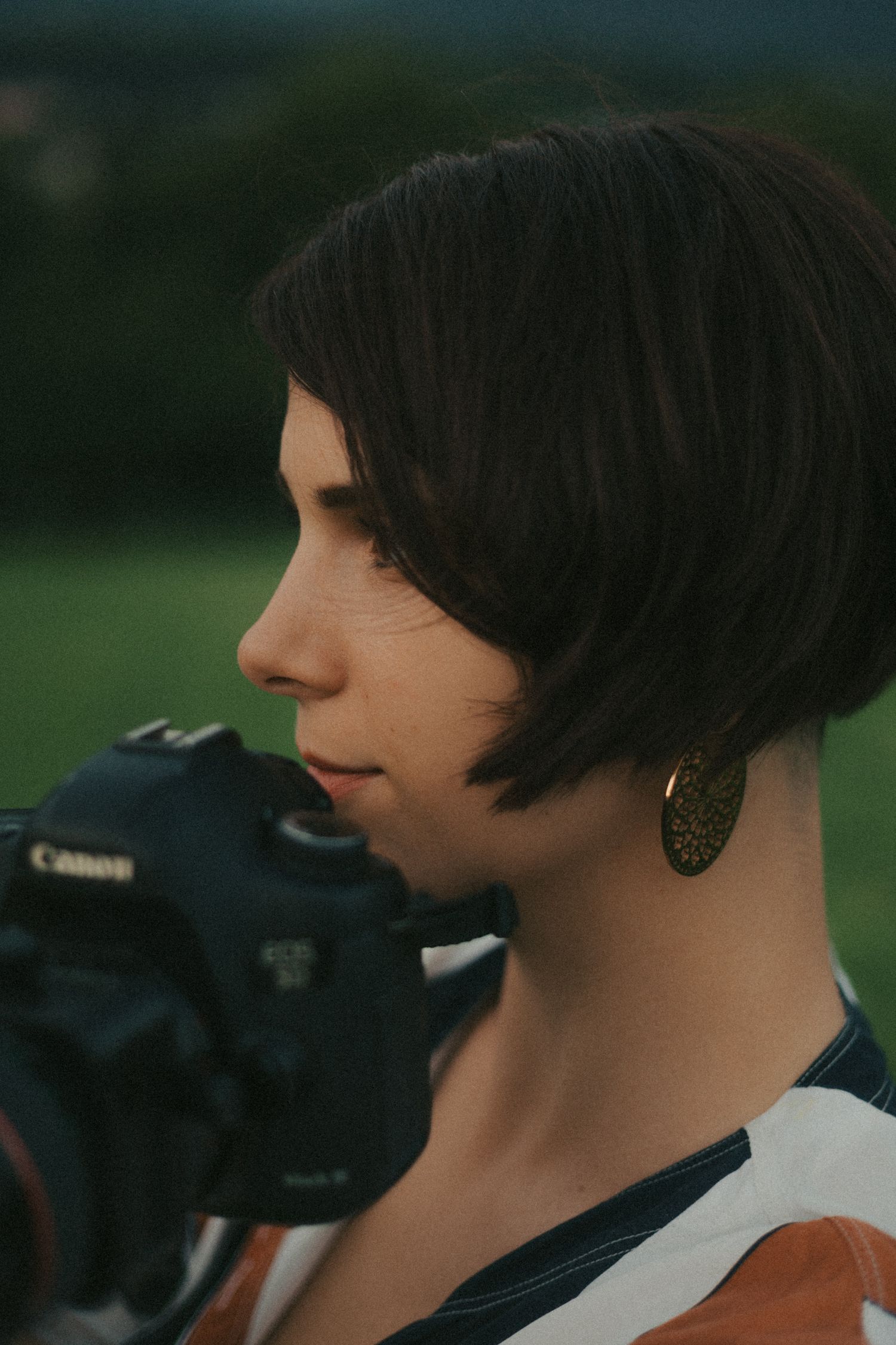 Une femme avec des cheveux courts foncés prend une photo à l'extérieur avec un appareil Canon en fin de journée