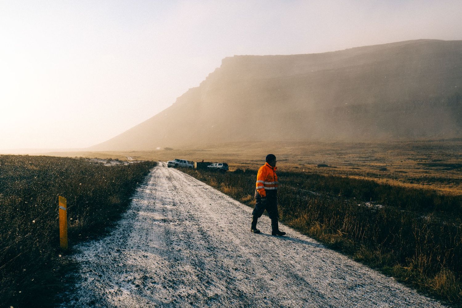 Worker in an orange vest standing on a gravel road in a misty Icelandic valley with dramatic mountain backdrop.