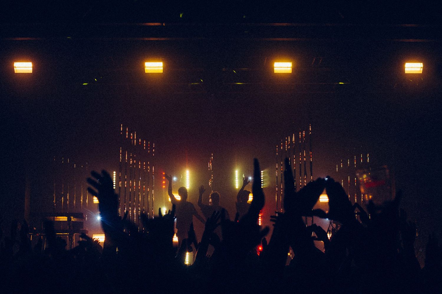 Energetic concert crowd with raised hands silhouetted against warm golden stage lighting.