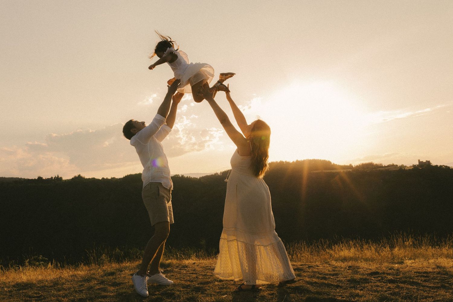 Parents lifting their young child into the air against a golden sunset in an open field.