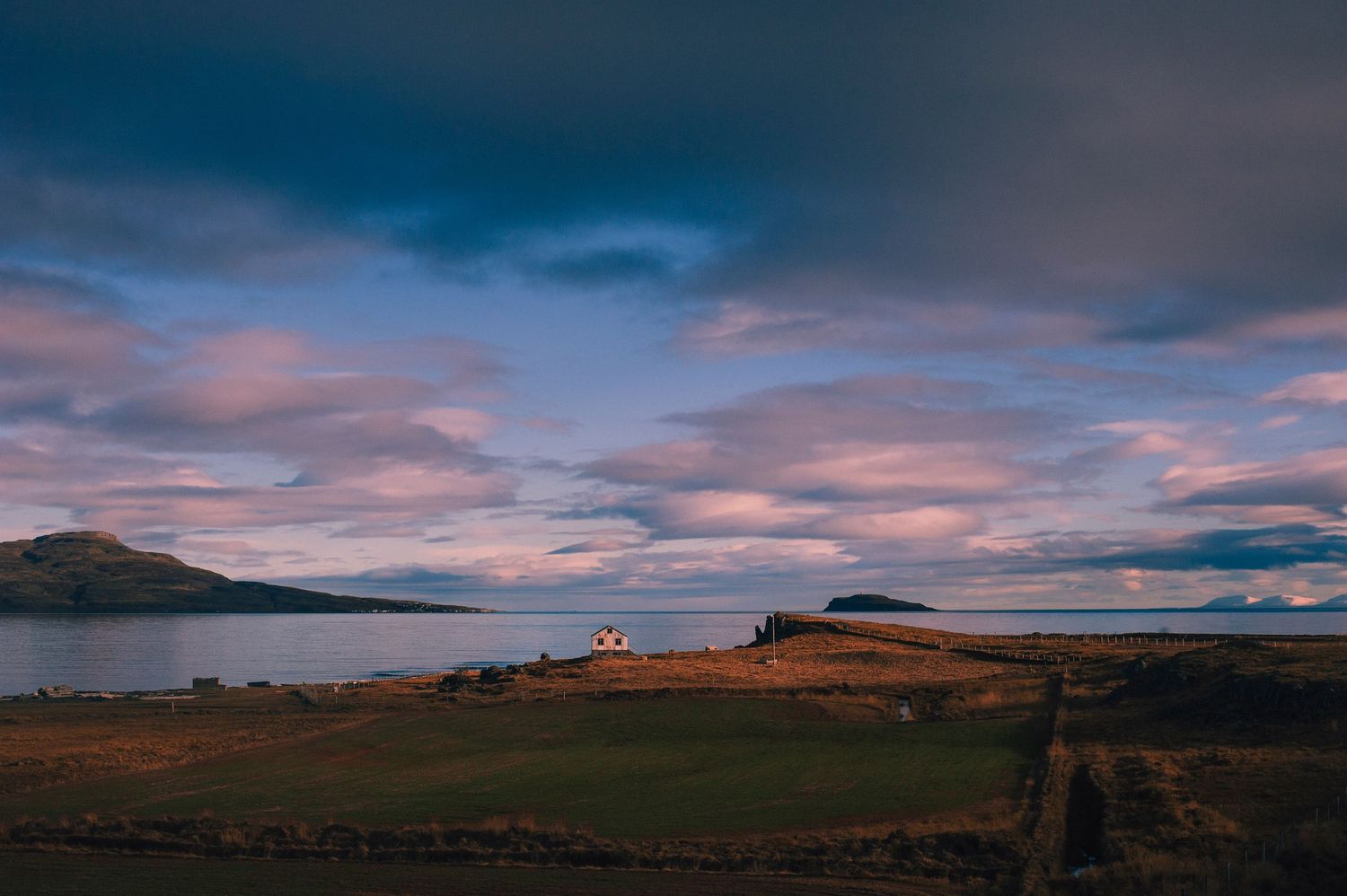 A dramatic sunset over a coastal Scottish landscape with a lone white cottage near the water.