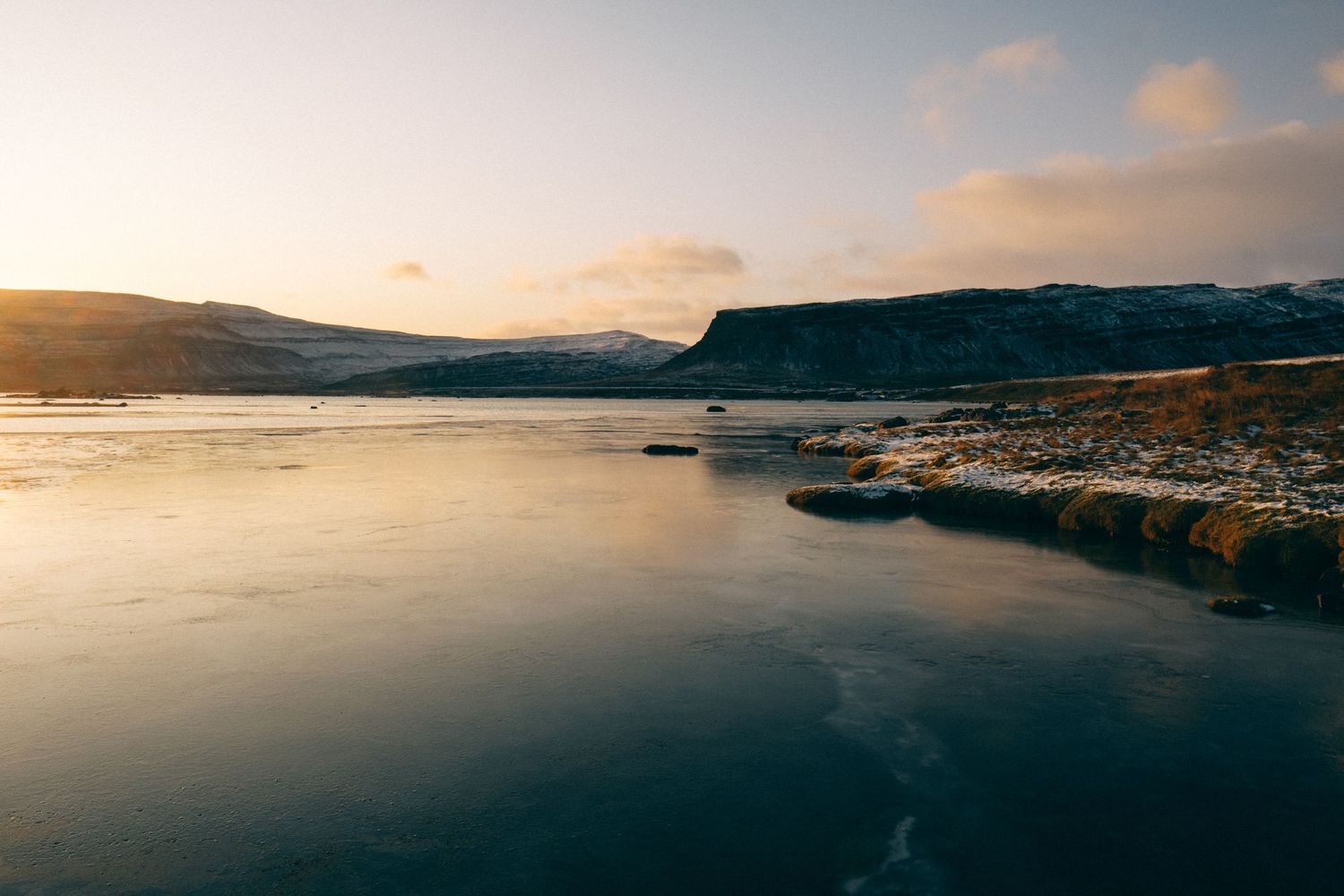 Fjord au paysage serein au coucher de soleil avec une couche de glace reflétant la lumière dorée et les monts enneigés