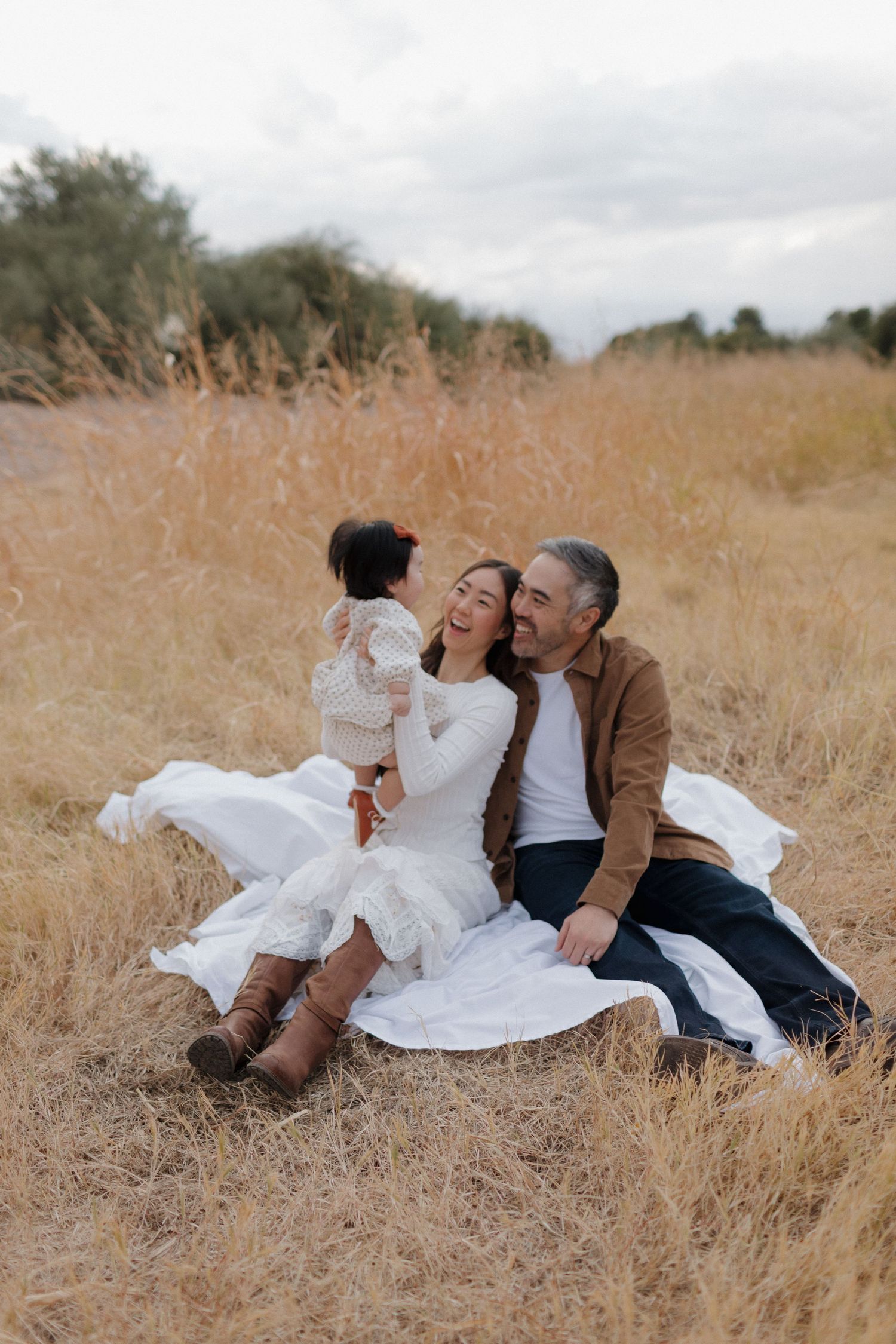 A small family lays together intimately in a golden autumn field during sunset.