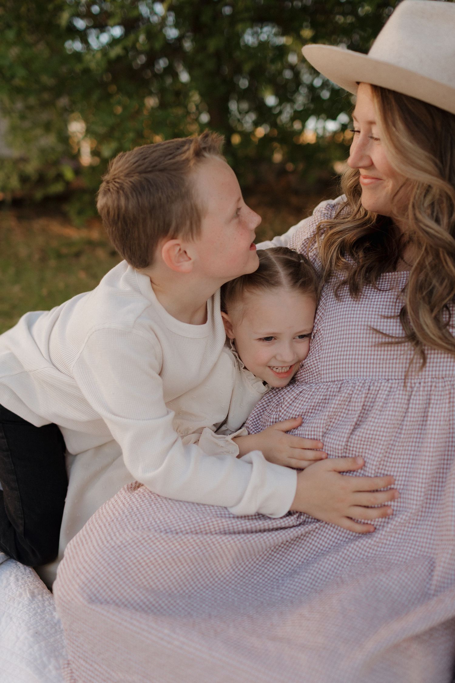 Family sharing tender moment outdoors on blanket during maternity photo session.