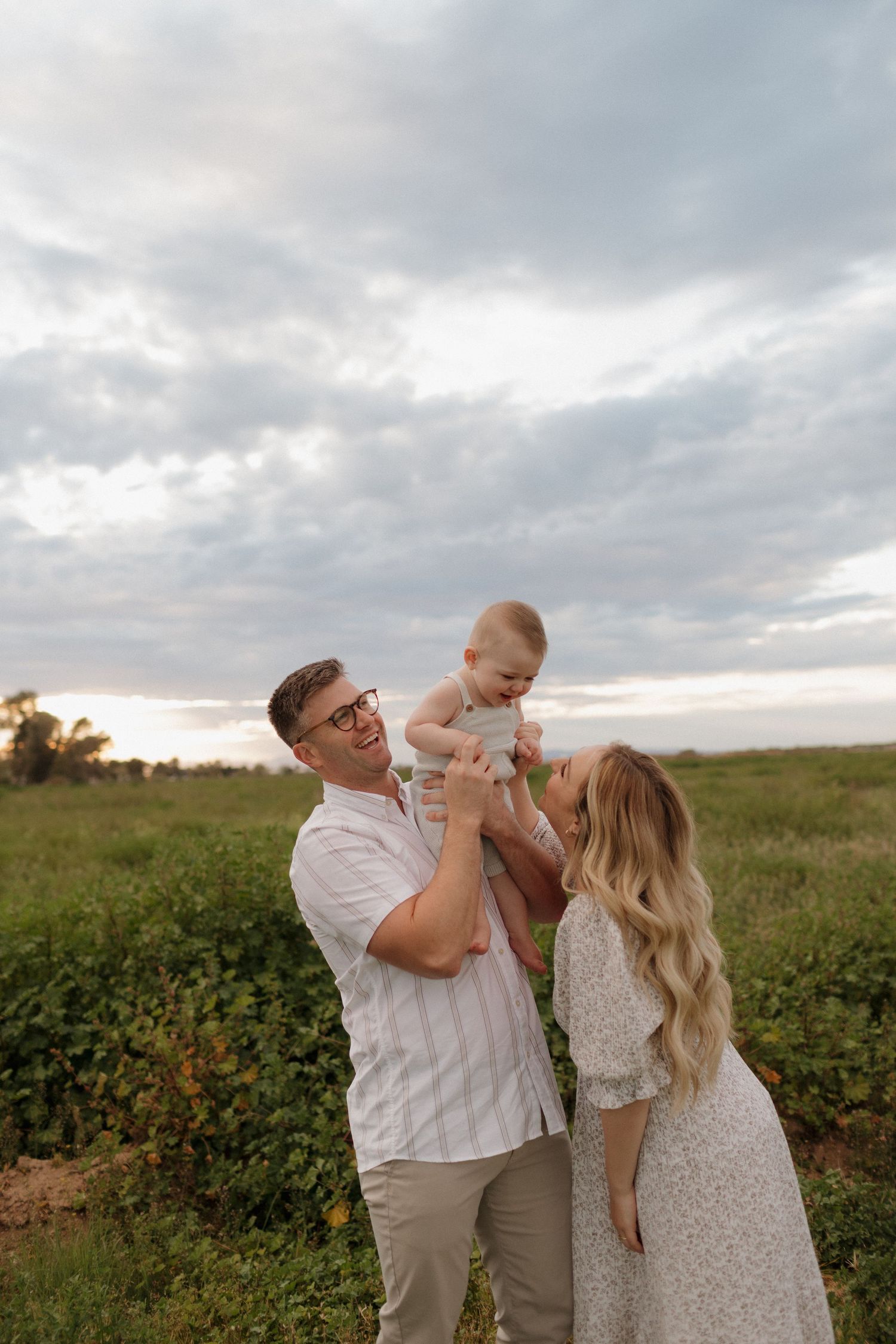 Parents playfully lift their baby in the air during a sunset photoshoot in a meadow.