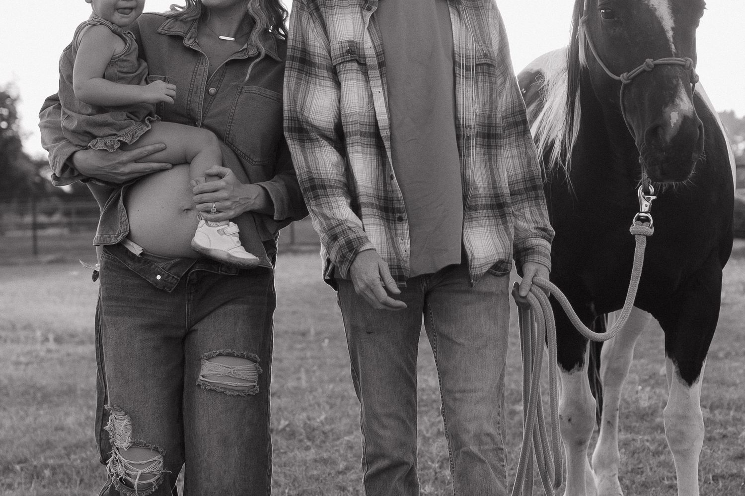 Black and white photo of a couple with a baby and a horse outdoors on a farm.
