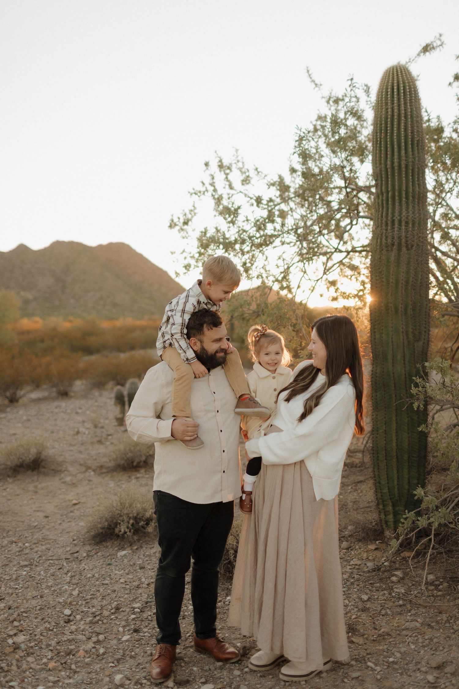Family of four poses near a tall saguaro cactus in the Arizona desert at golden hour sunset.