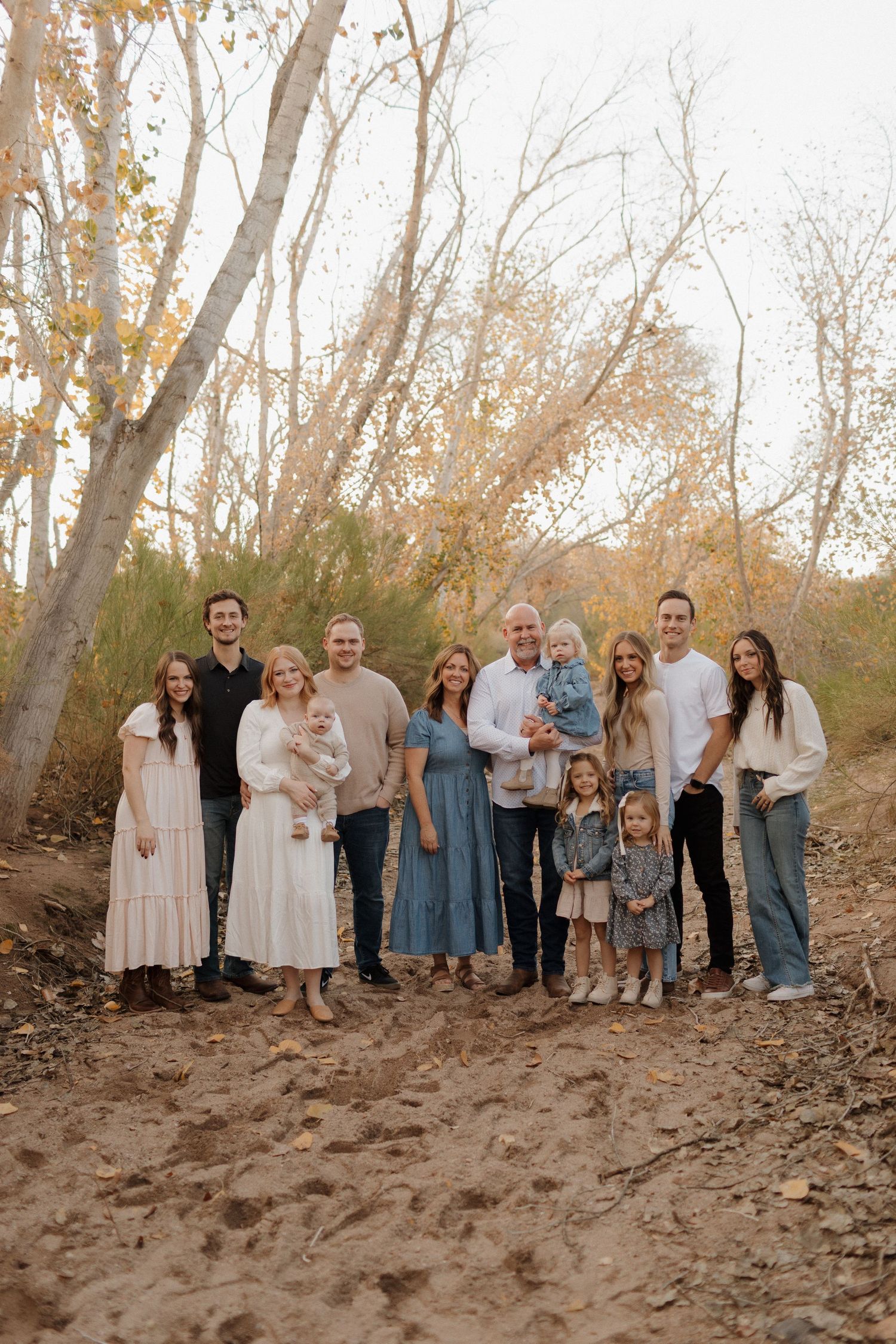 A group of people wearing coordinated neutral and blue outfits pose together outdoors in a wooded autumn setting.