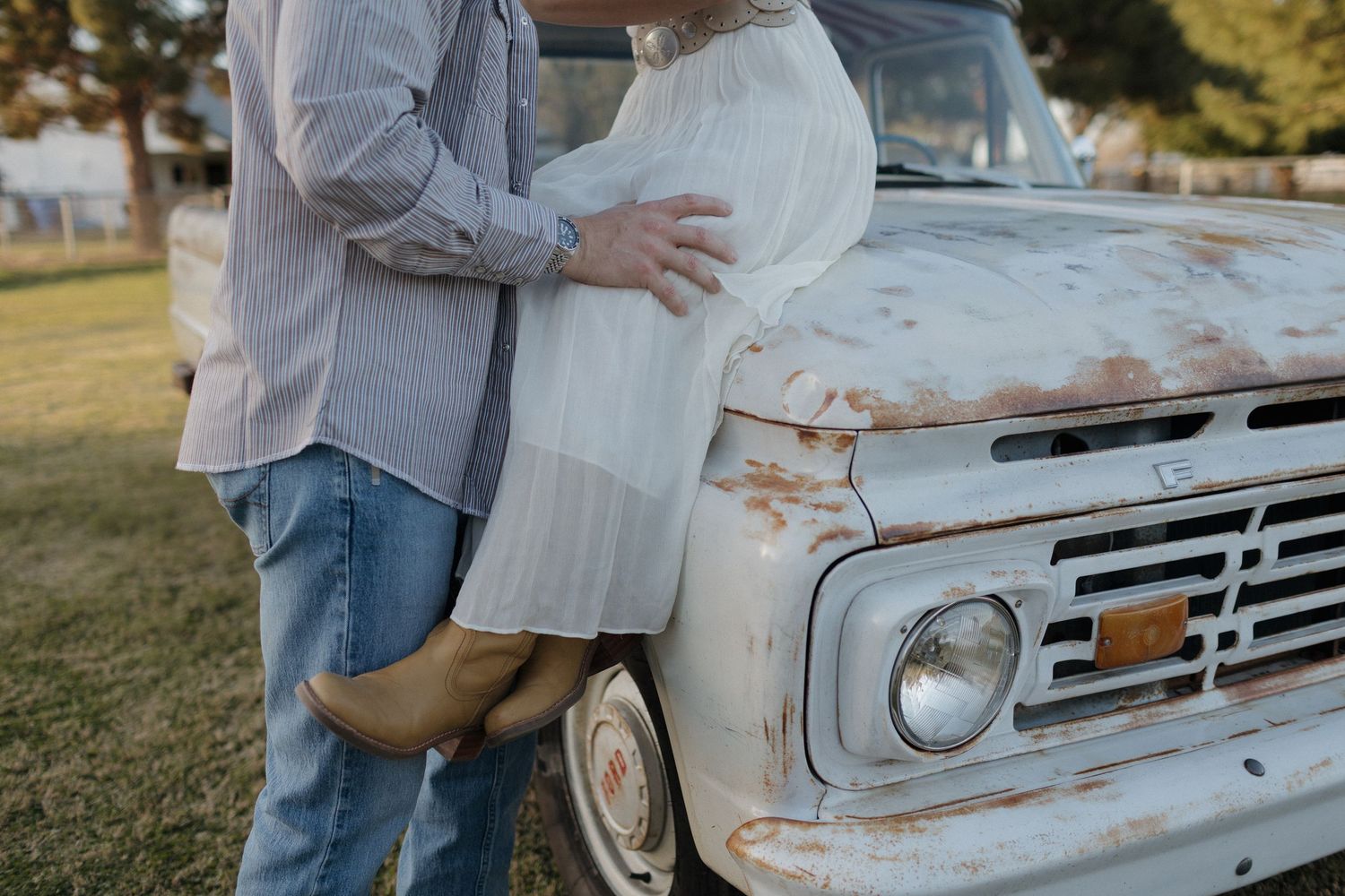 A couple poses together near a vintage white pickup truck in a grassy field during golden hour.