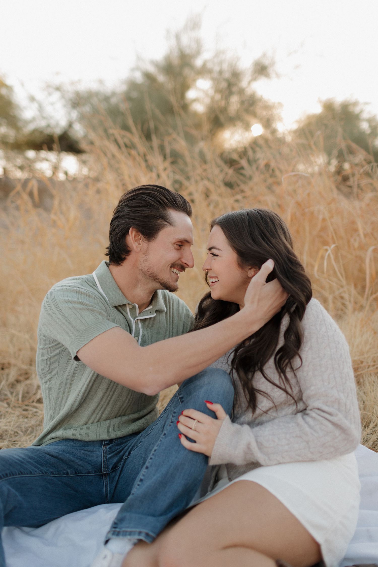 A couple shares an intimate moment sitting on a blanket in a field during golden hour.