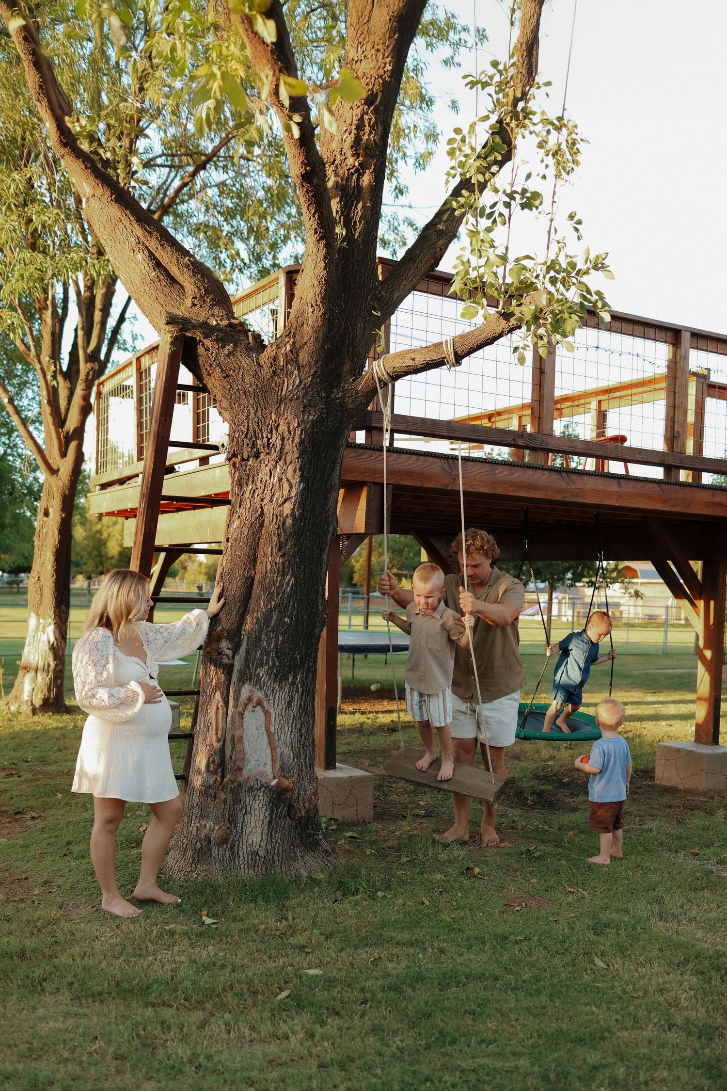 A series of photos showing people building and installing a wooden treehouse platform between mature trees in a backyard.
