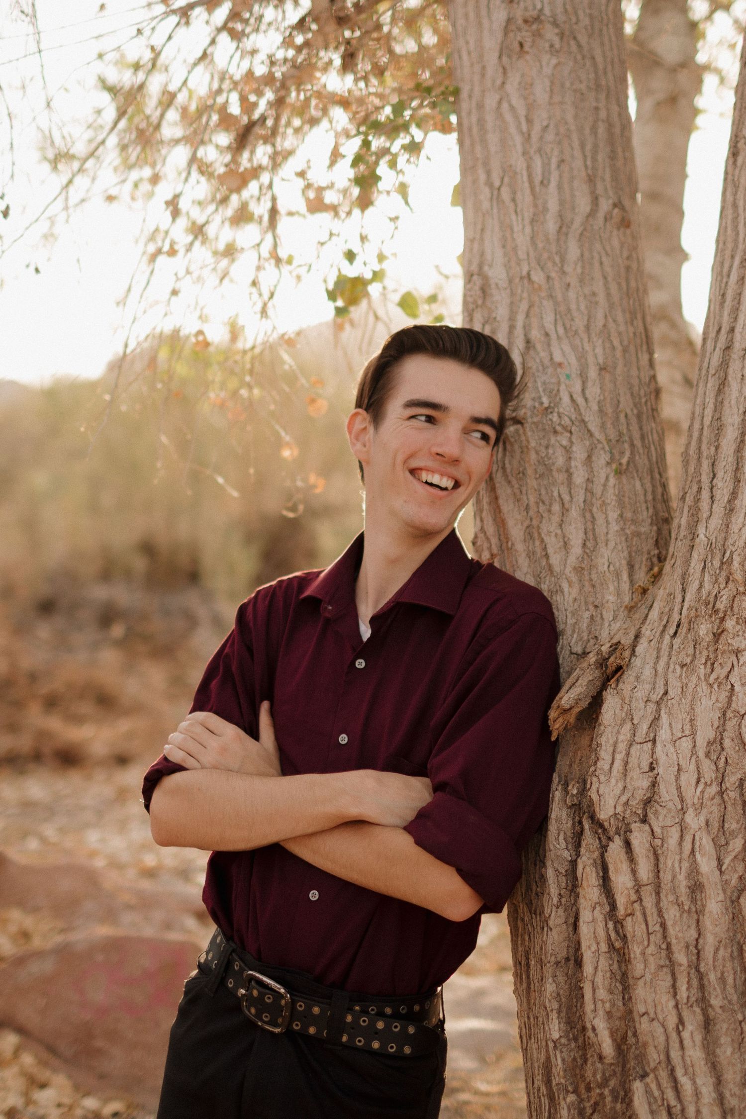Warm sunset graduate portrait against rustic tree trunk in desert setting.