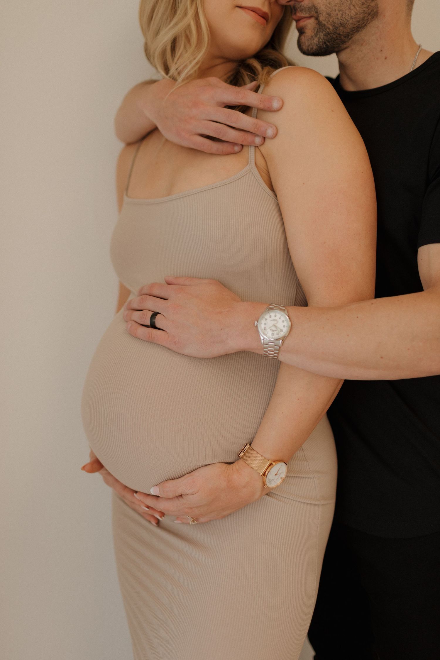 Intimate maternity portrait showing pregnant belly in form-fitting beige dress.
