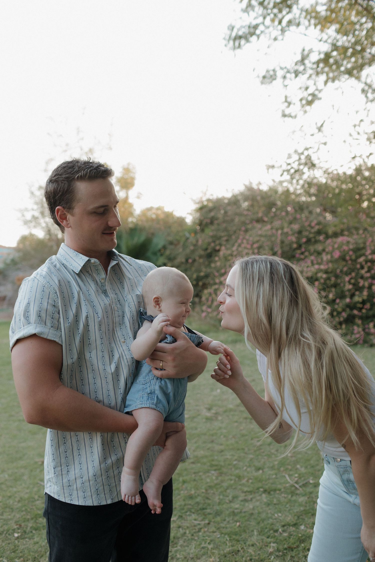 Parents with baby outdoors share tender moment in evening light.