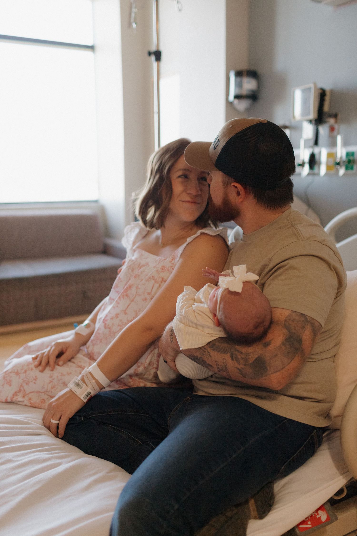 A family at the hospital shares an intimate moment admiring their new baby girl with soft natural light coming through the windows.