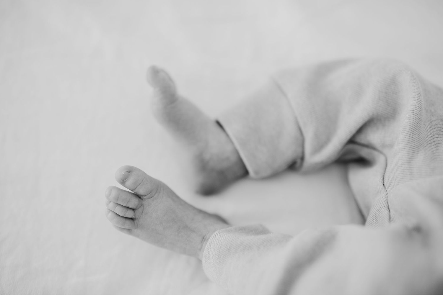 Black and white detail of infant's tiny foot against white fabric.
