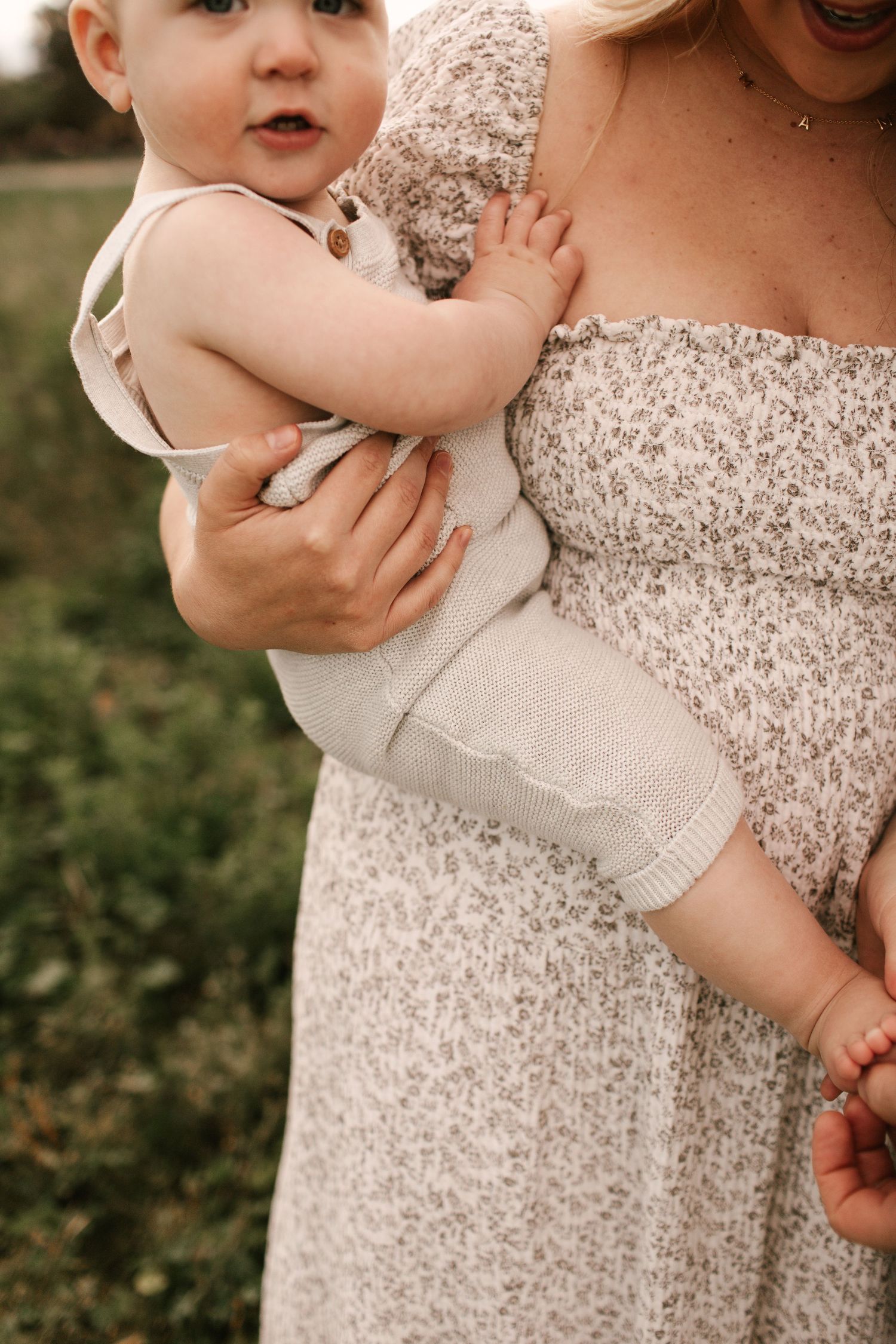 Young child in light colored outfit being held against floral patterned dress.