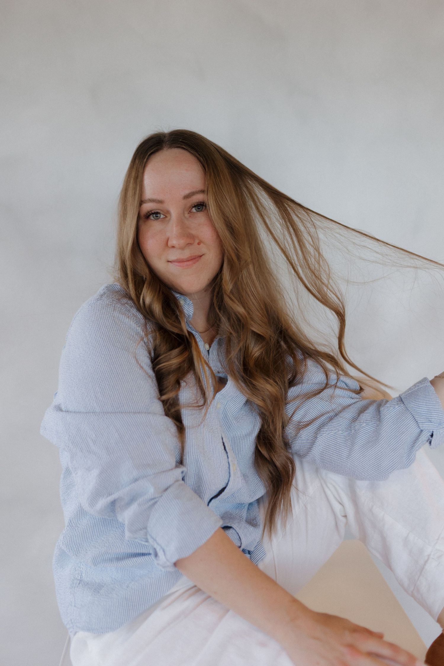 Photographer in a light blue button-up shirt poses with flowing long brown hair against a white background.