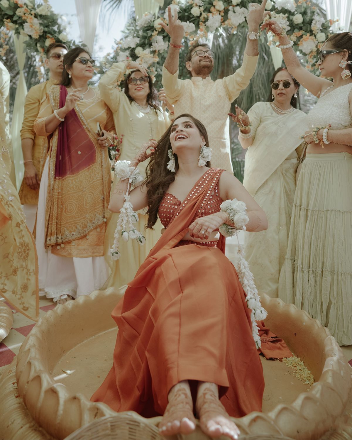 Wedding celebration scene with guests in traditional attire gathered around decorated floral setting.