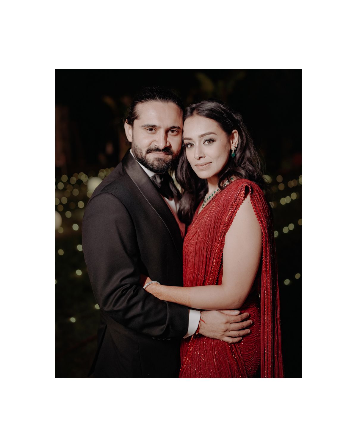 A couple poses together at an evening event, with her wearing a red gown and him in a dark suit.