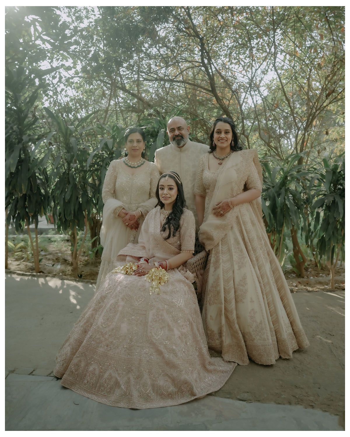 A small group poses together in coordinated cream-colored formal attire for a wedding portrait outdoors.