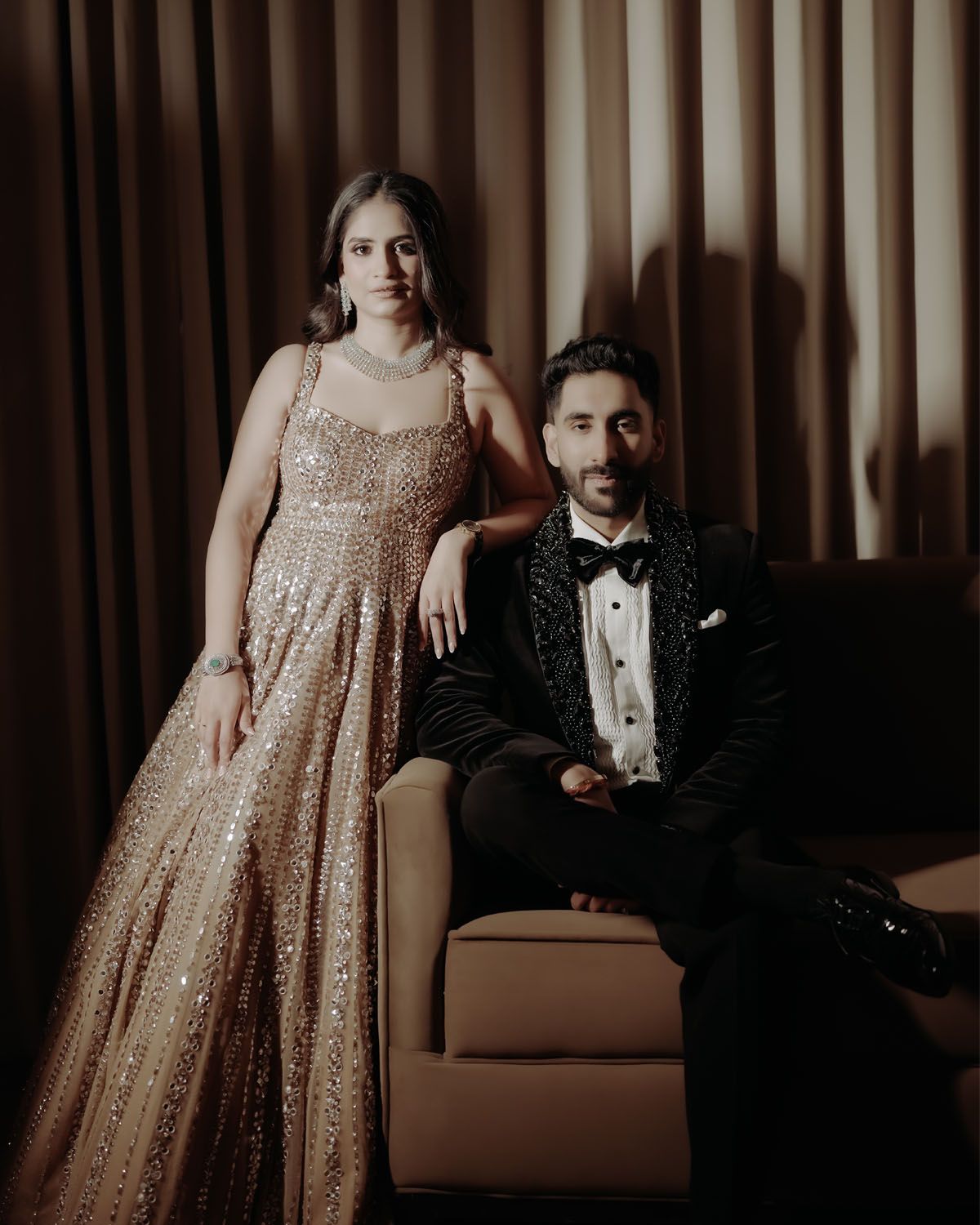 Couple in formal attire posing on couch with woman in sparkly gold gown and man in black tuxedo.
