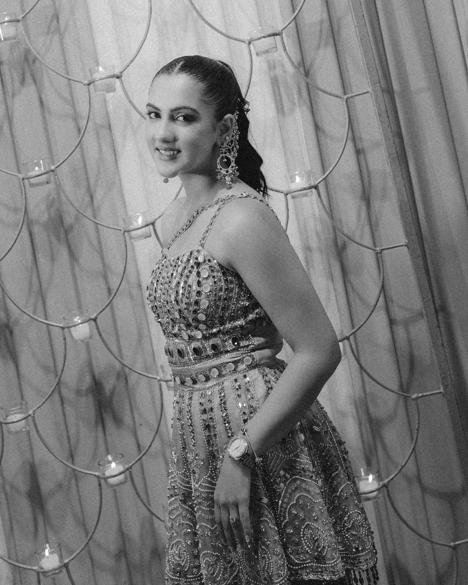 Black and white photo of a woman in an embellished dress with chandelier earrings, posing elegantly indoors.