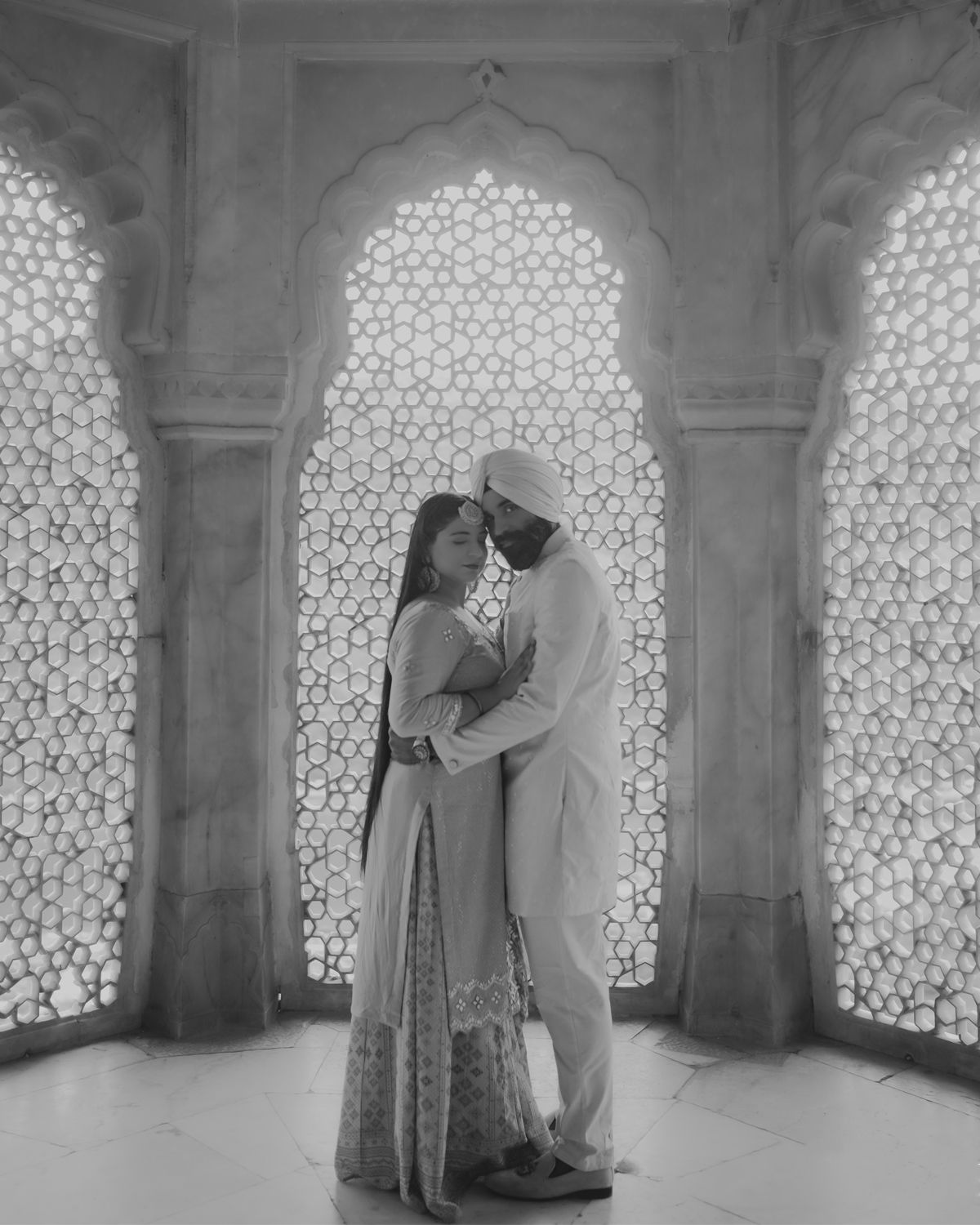 A romantic embrace between two people standing in an ornate archway with intricate lattice screens.