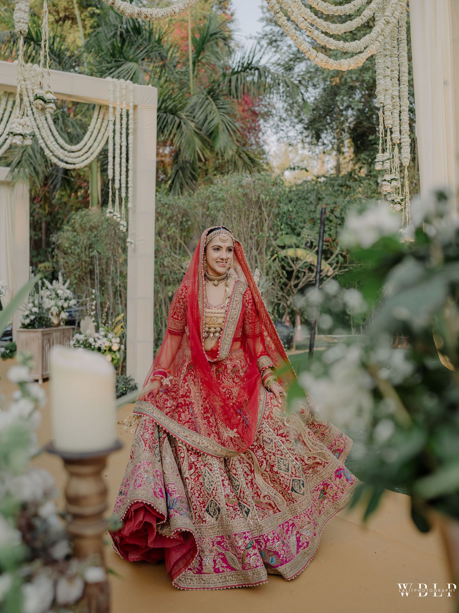 Indian bride in red lehenga twirling at outdoor wedding ceremony with floral decorations.