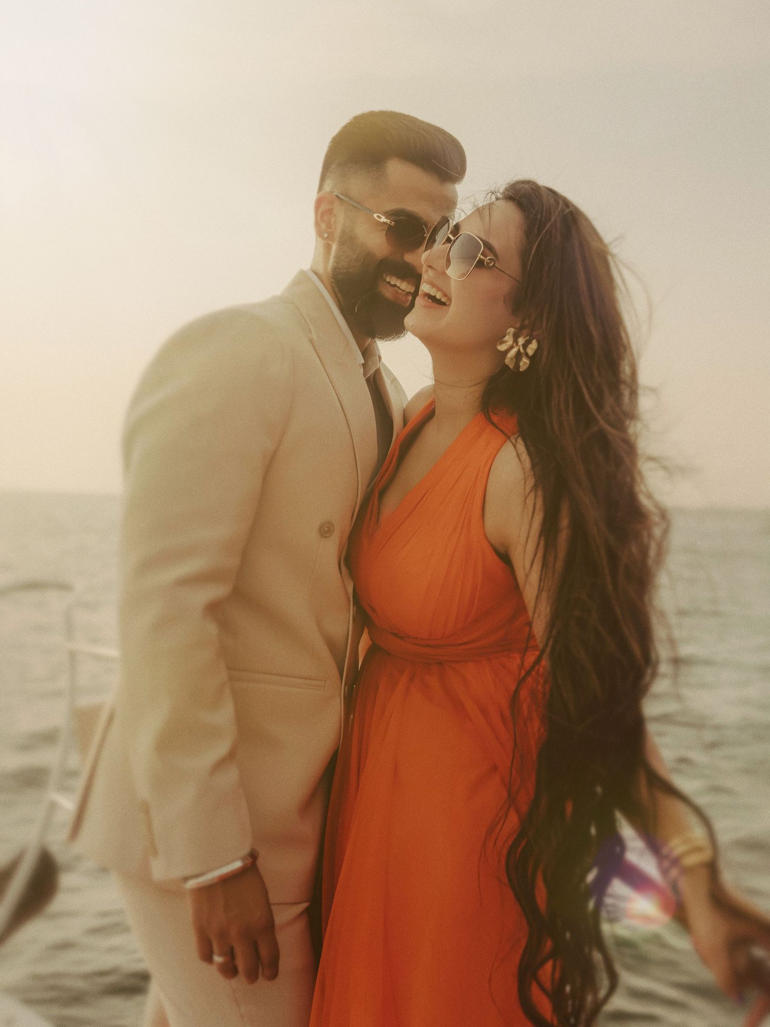 Couple in elegant attire sharing a romantic moment on a boat, woman in orange dress, man in white suit.