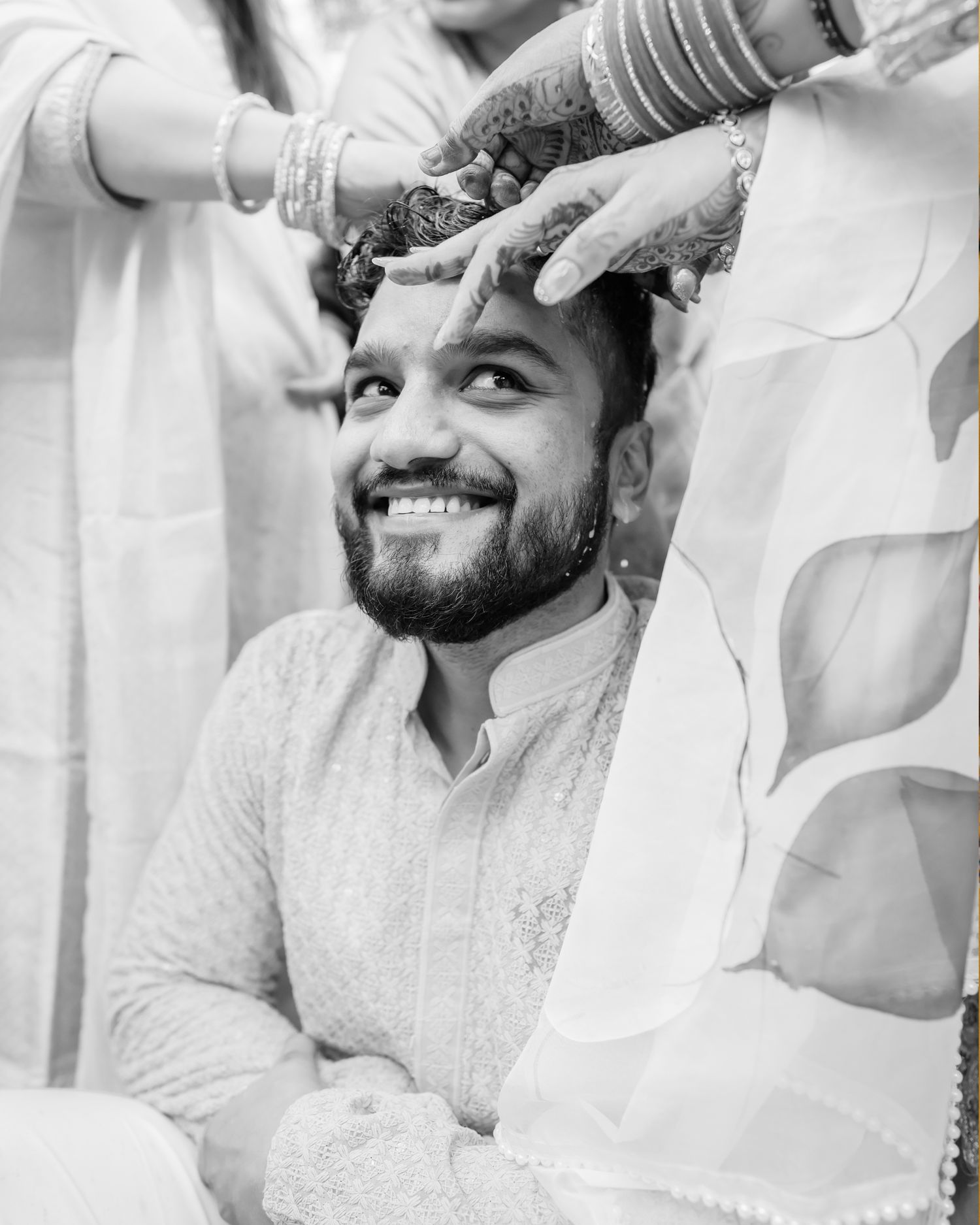 Black and white photo of a smiling bearded groom in kurta during an Indian wedding ceremony.