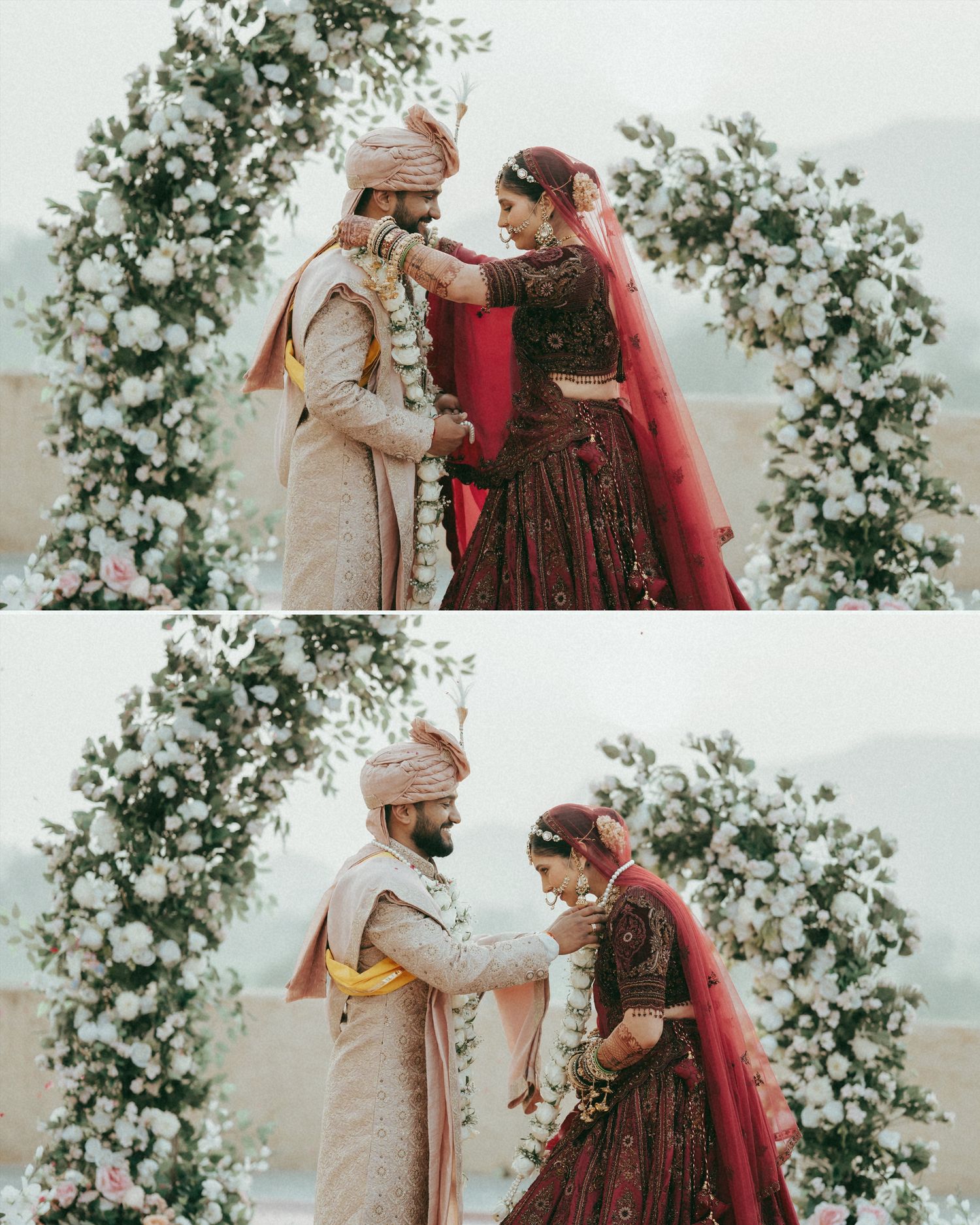 Indian bride in red lehenga and groom in pink sherwani exchange garlands under a floral arch at a traditional wedding.