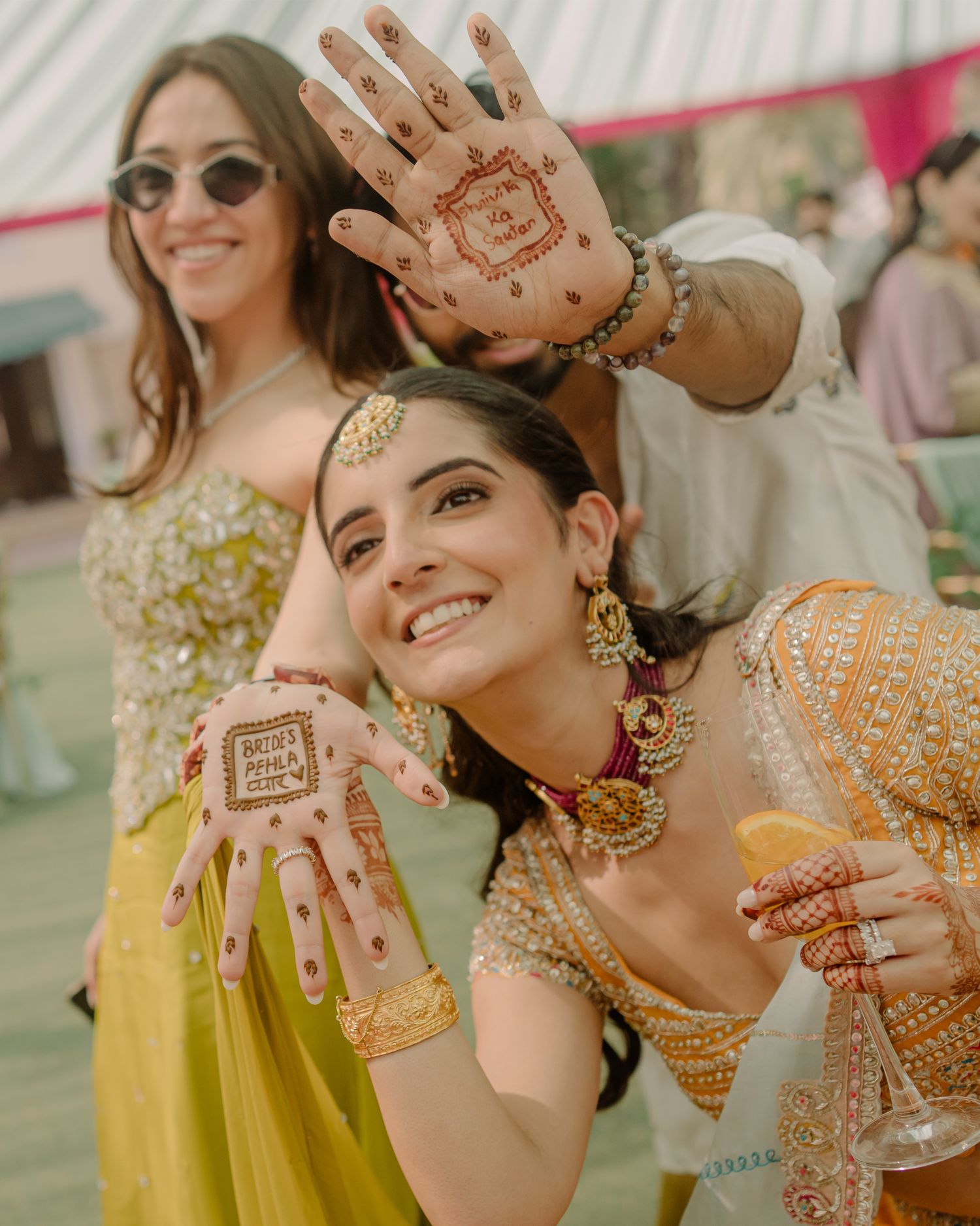 Bride showcasing intricate mehndi henna designs on hands at a colorful Indian wedding celebration.