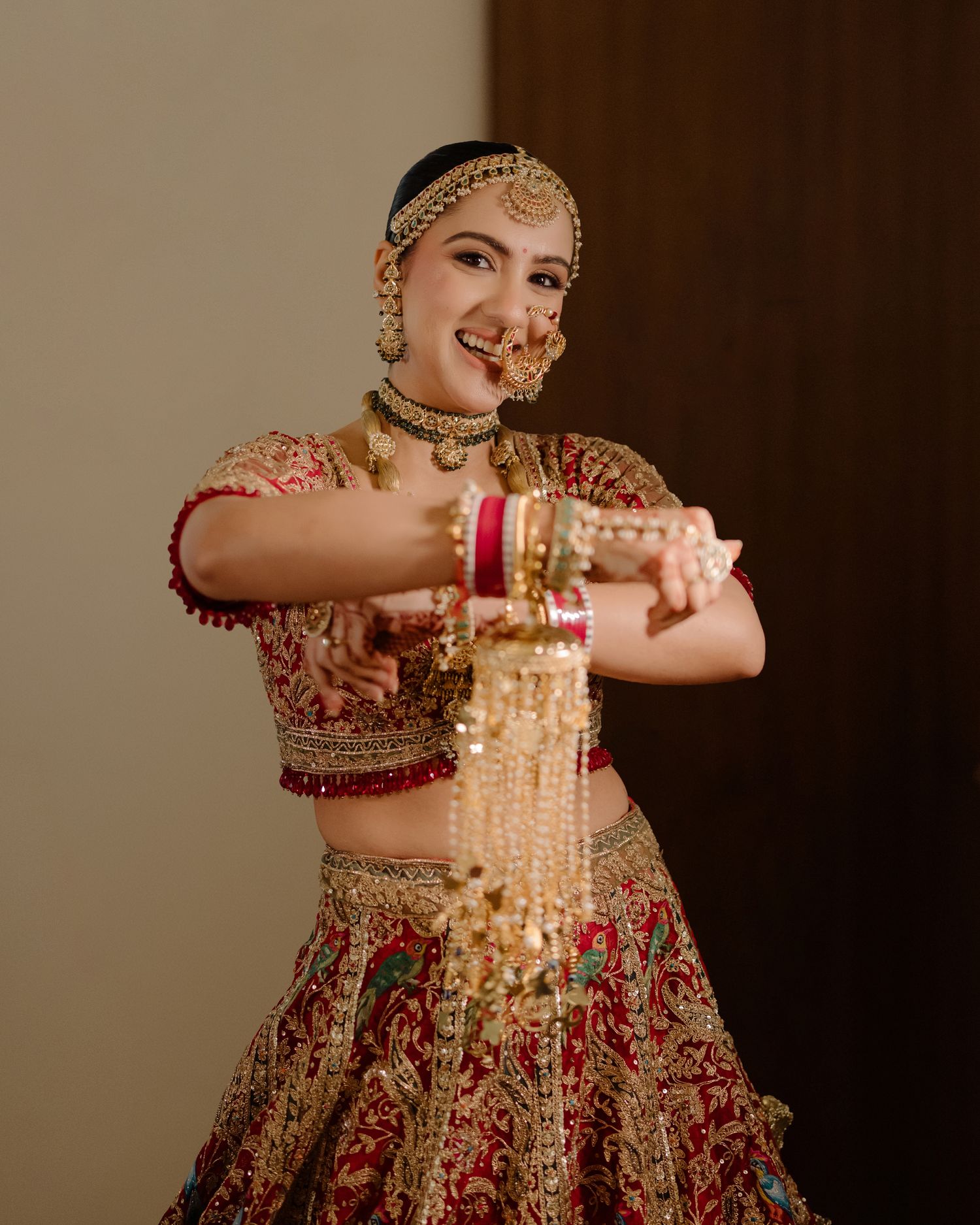 Bride in red and gold lehenga with traditional jewelry dancing joyfully at an Indian wedding celebration.
