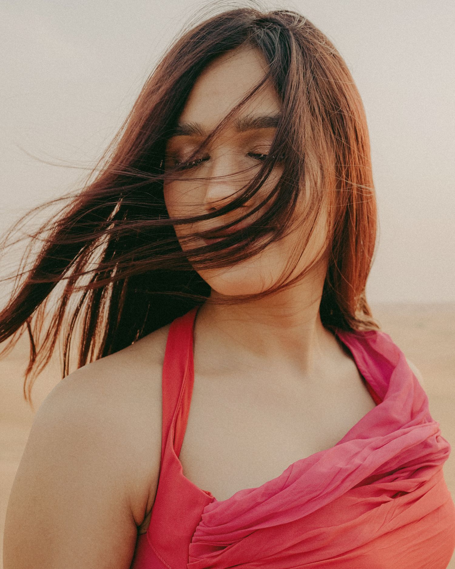 Woman in pink dress with hair blowing across her face in a dreamy outdoor desert setting.